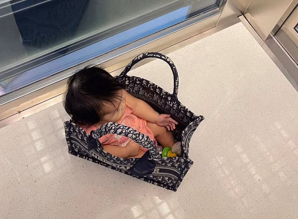 Cô bé ngồi lọt thỏm trong túi xách của mẹ.