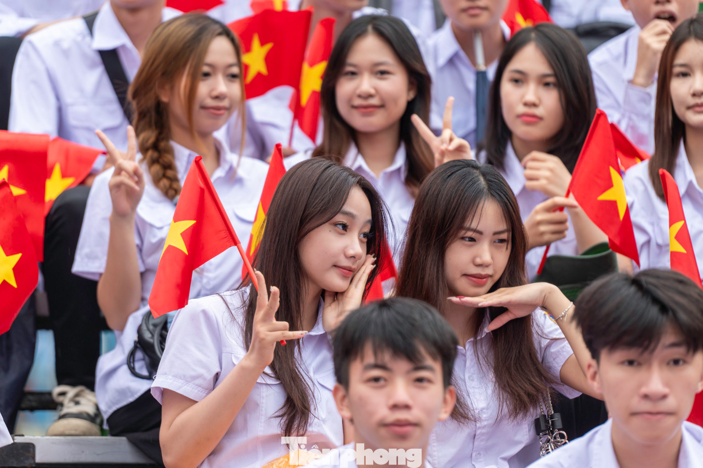 Các em học sinh, sinh viên mặc đồng phục áo trắng, tay cầm cờ đỏ sao vàng trên khán đài.