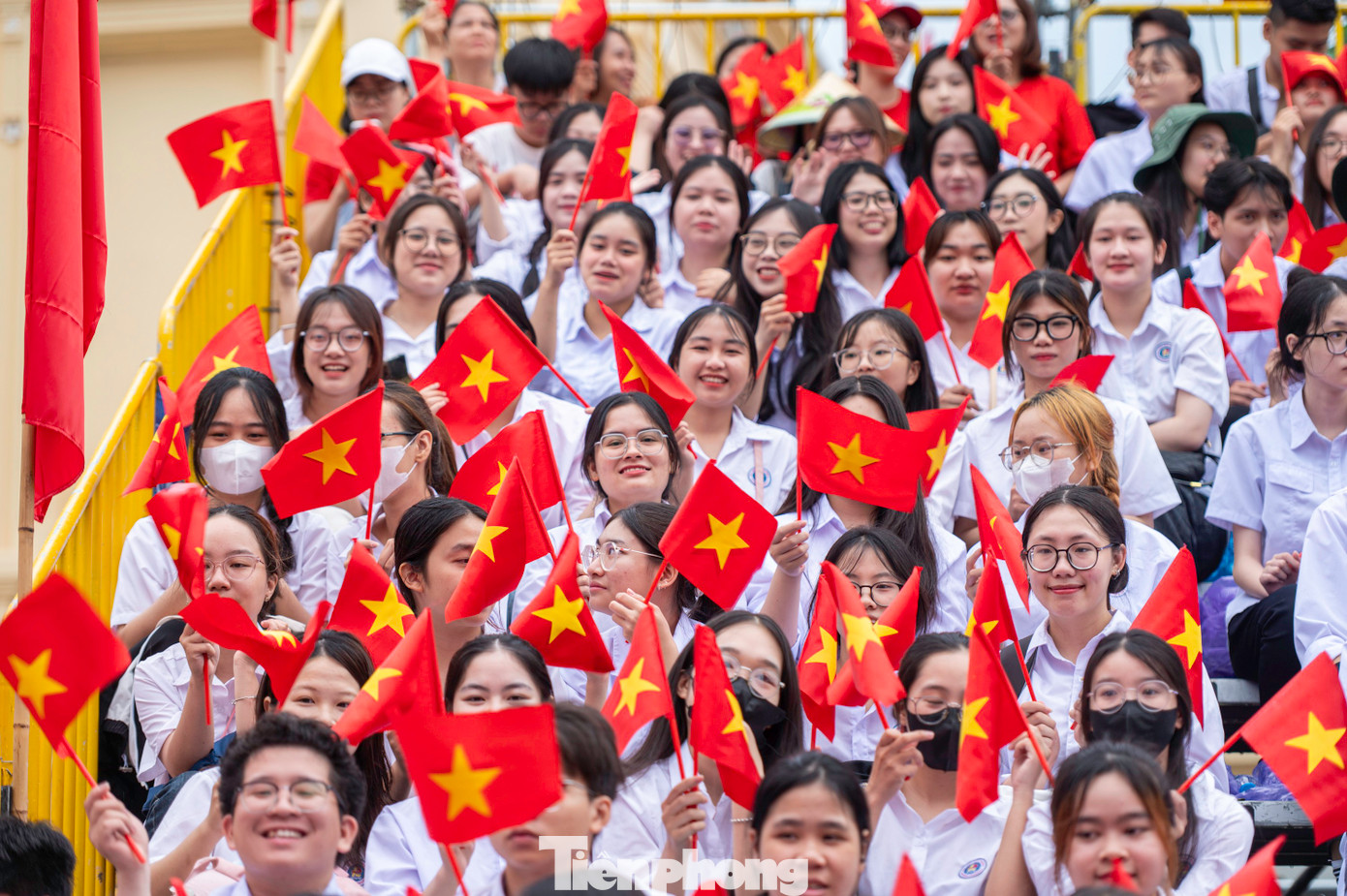 Các em học sinh, sinh viên mặc đồng phục áo trắng, tay cầm cờ đỏ sao vàng trên khán đài.