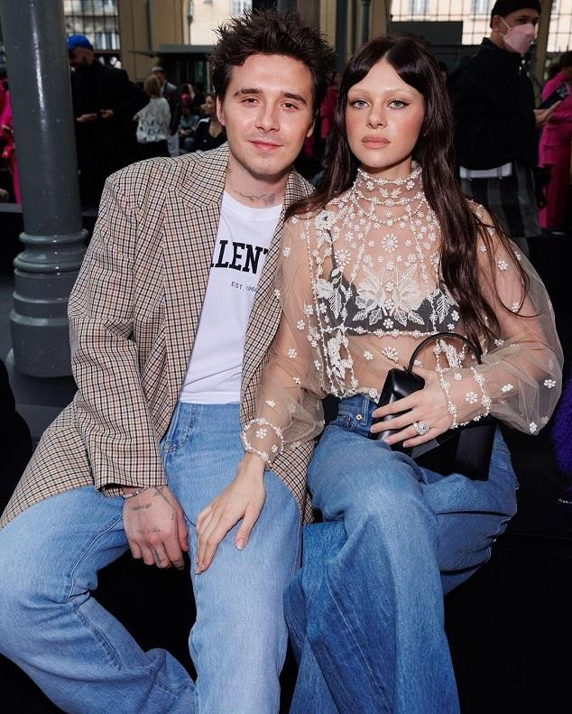 Brooklyn kết hợp áo phông trắng in chữ thương hiệu, quần jean ống rộng, blazer kẻ và giày da đen độn đế.