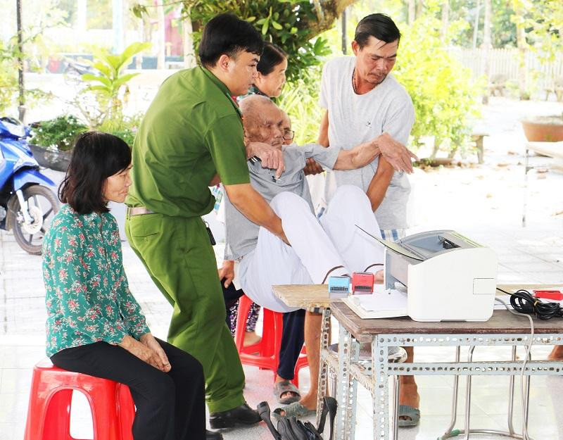 Một cụ già đi lại khó khăn được hỗ trợ lấy vân tay.