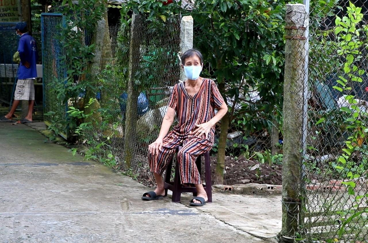 Một cụ bà ngồi trước nhà chờ xe lấy mẫu xét nghiệm đến - Ảnh: Kim Hà.