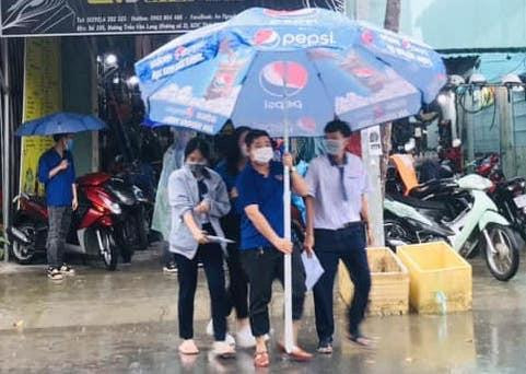 Tình nguyện viên che dù cho thí sinh đến điểm thi trong cơn mưa to.
