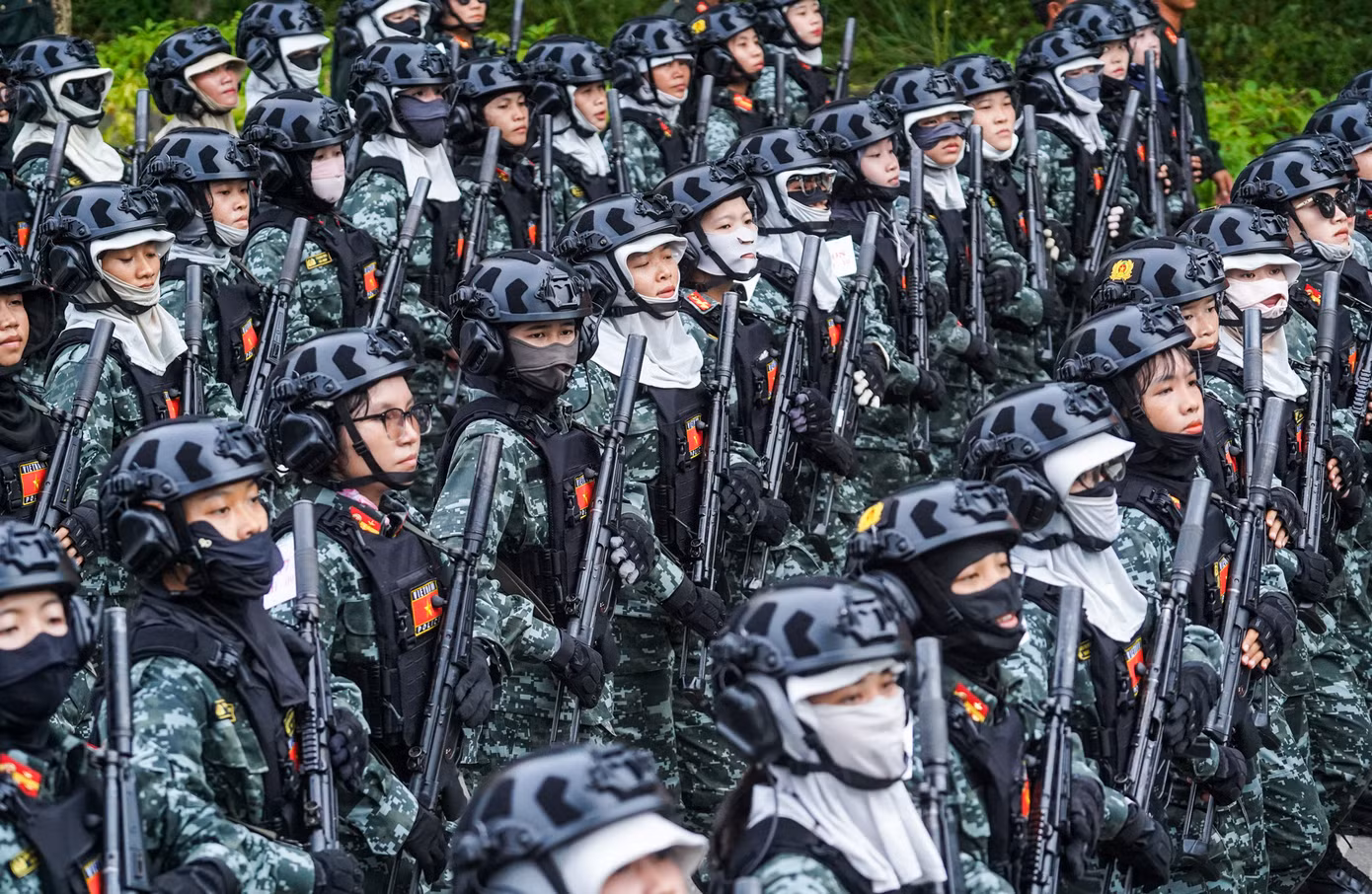 Khối nữ chiến sĩ cảnh sát đặc nhiệm mặc quân phục ngụy trang kỹ thuật số màu xanh rêu, đội mũ bảo hiểm đen gắn bộ đàm, đeo áo giáp mềm và trang bị súng tiểu liên MP5.