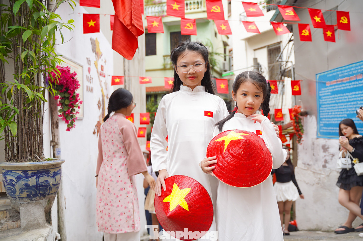 Hai em bé mặc áo dài cầm trên tay nón lá hình Quốc kỳ chụp hình tại ngõ cờ hoa Yên Phụ.