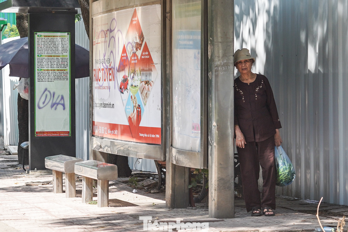 Hành khách đứng đợi xe buýt núp sau trạm nhà chờ để "trốn" nắng.