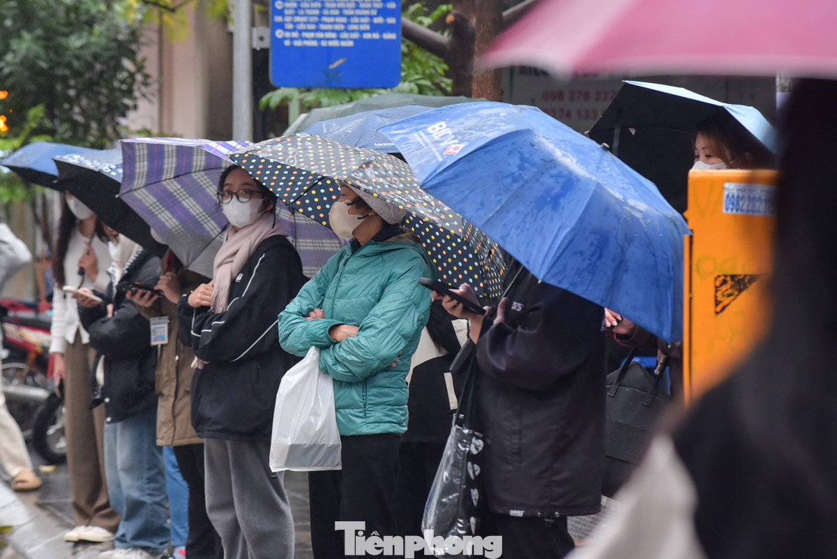 Người dân cầm ô che mưa chờ xe buýt trong tiết trời u ám.