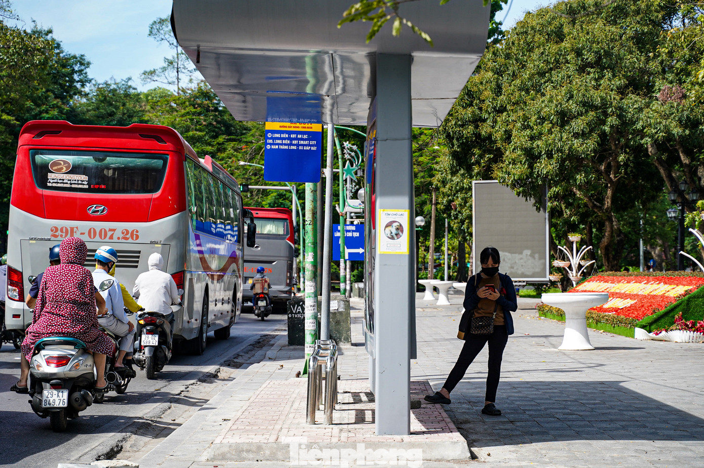 Hành khách đứng đợi xe buýt núp sau trạm nhà chờ để tránh nắng.