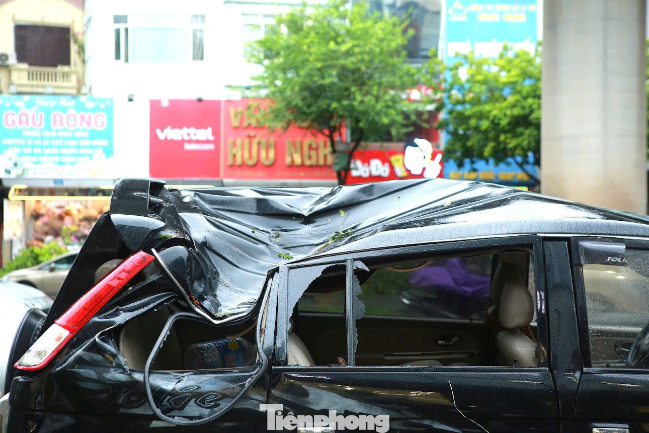 Chiếc xe ô tô bị hư hỏng nặng, vỏ xe bị móp méo nghiêm trọng do bị cây đổ đè trúng trên phố Trần Đăng Ninh.