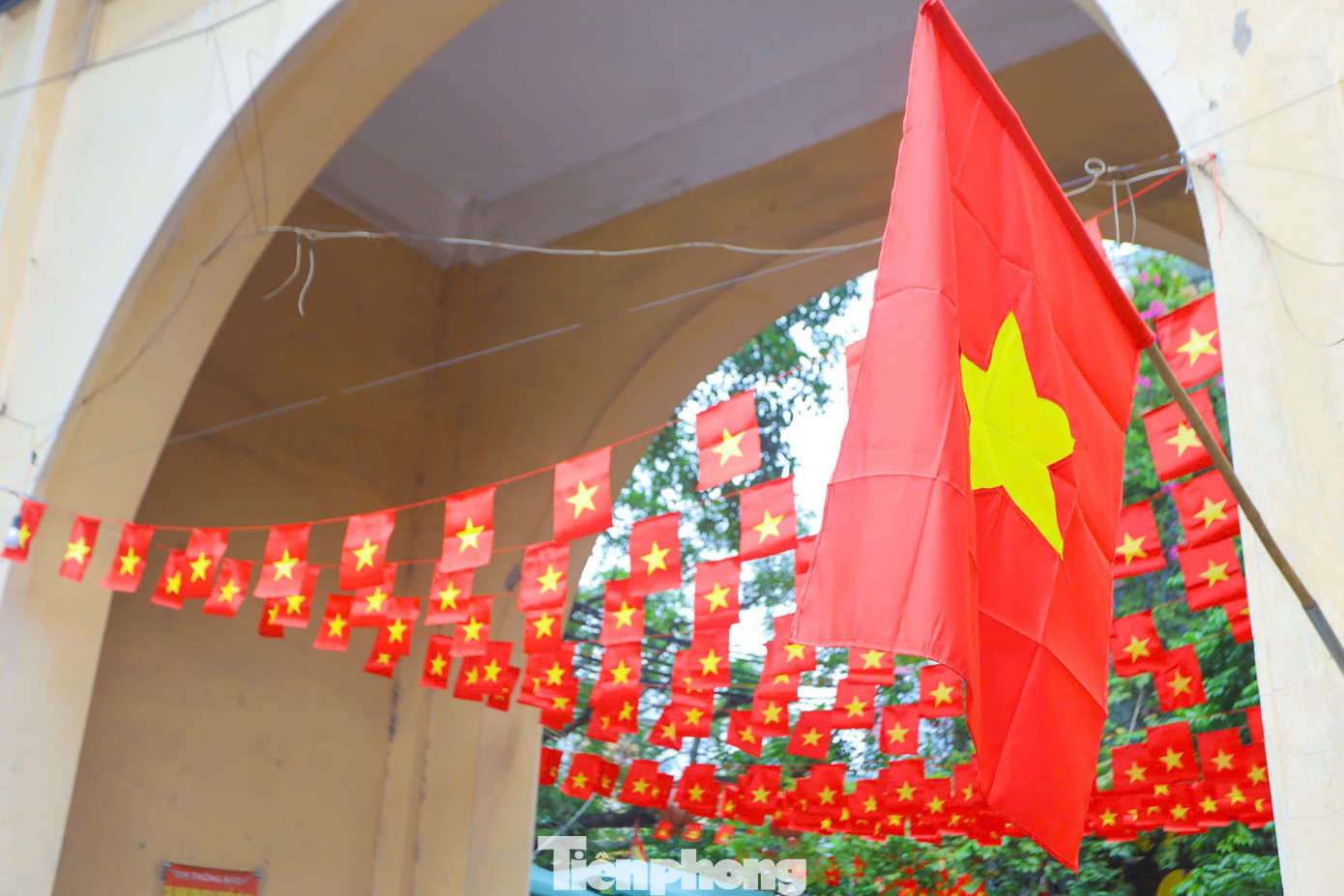 Màu cờ đỏ rực nổi bật trên cổng làng cổ kính và màu xanh của cây cối tạo nên một khung cảnh đẹp mắt.