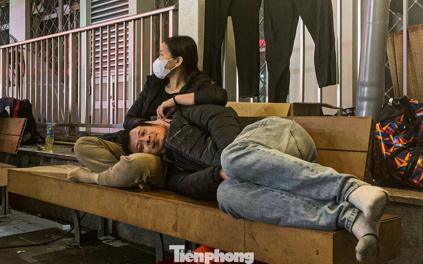 Người đàn ông nằm co ro trên chân vợ phía bên ngoài đối diện Trung tâm cấp cứu A9 Bệnh viện Bạch Mai. "Tôi và vợ đã đến đây chăm sóc mẹ bị bệnh suốt mấy hôm rồi. Thời tiết rét buốt như này khiến chúng tôi gặp rất nhiều khó khăn, không chỉ vì cái lạnh mà còn vì phải chờ đợi trong khi lo lắng cho sức khỏe của mẹ."