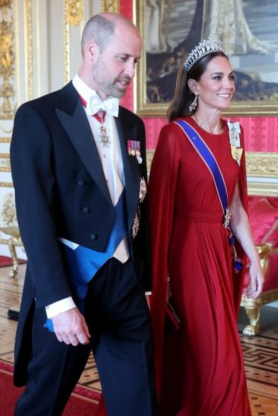 Trang sức đi kèm cũng được nâng cấp. Cô sử dụng hoa tai Greville Chandelier của cố nữ hoàng và đội vương miện Cambridge Lover's Knot Tiara, từng thuộc về Công nương Diana. Vòng tay ngọc trai ba sợi Nigel Milne cũng nằm trong bộ trang sức của mẹ chồng Kate. Trang phục còn kèm theo dải băng màu xanh và một số huy hiệu đại diện cho Hoàng gia Anh. Ảnh: Getty Images.