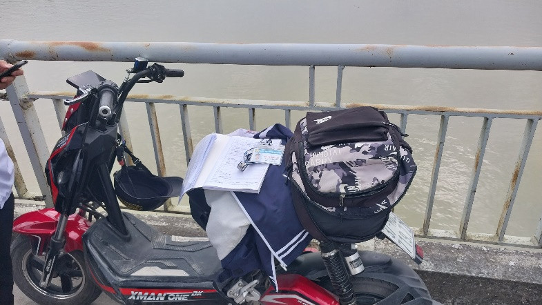 Xe máy điện cùng áo đồng phục, cặp sách, điện thoại của em T. ở trên cầu.