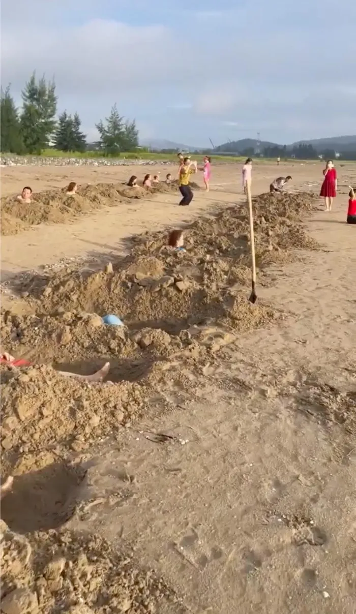 Hình ảnh nhóm du khách đào những hố hình giống "huyệt mộ" rồi tắm cát. (Ảnh cắt từ clip).