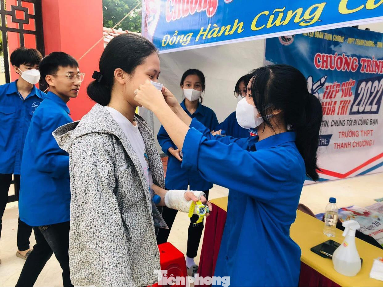 Một thí sinh bị thương ở tay được tình nguyện viên phát và đeo khẩu trang trước khi vào phòng thi