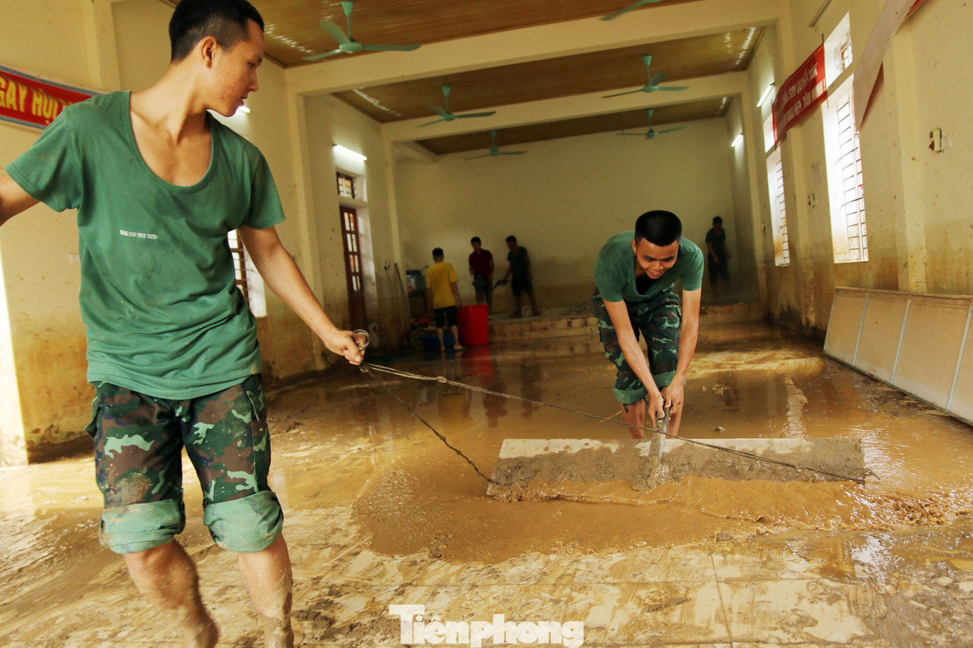 Phía bên trong nhà văn hóa cộng đồng, do bùn lầy bám chặt lâu ngày nên lực lượng phải vừa bơm nước rửa sạch, vừa đẩy bùn ra ngoài.
