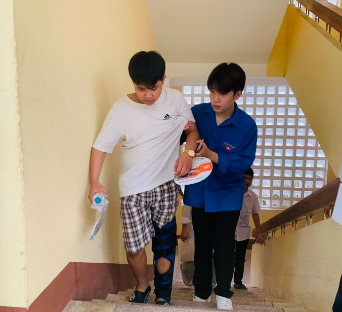 1 học sinh dự thi tại điểm thi THPT Hoài Đức B, huyện Hoài Đức bị đau chân phải nhờ đến sự trợ giúp của lực lượng thanh niên tình nguyện.