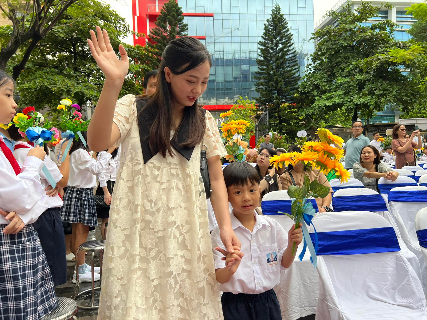 Học sinh lớp 1 tay cầm hoa được bố mẹ dắt lên sân khấu trong sự chào đón của anh chị lớp trên và thầy cô giáo.