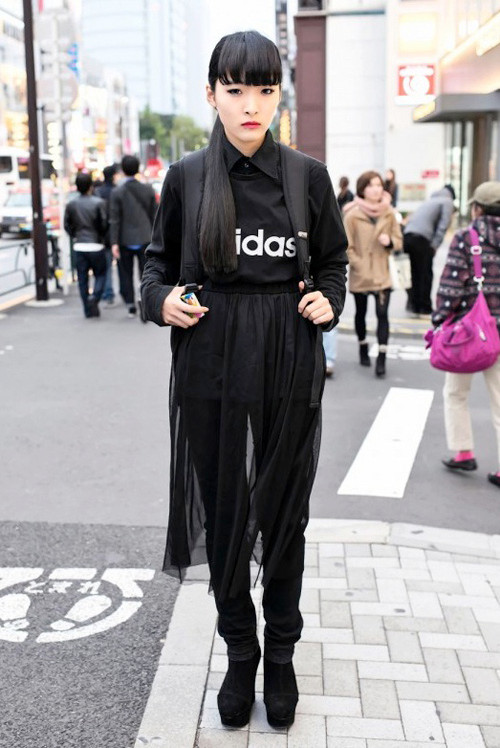 Chiki Chiki (17 tuổi) nổi bần bật trên phố đông với cả cây đen tông xuyệt tông từ đầu đến chân. Cô nàng mix áo phông Adidas, sơ mi đen cài kín cổ cùng quần jeans. Chiếc váy xuyên thấu dài quá gối layer bên ngoài giúp tổng thể thêm 