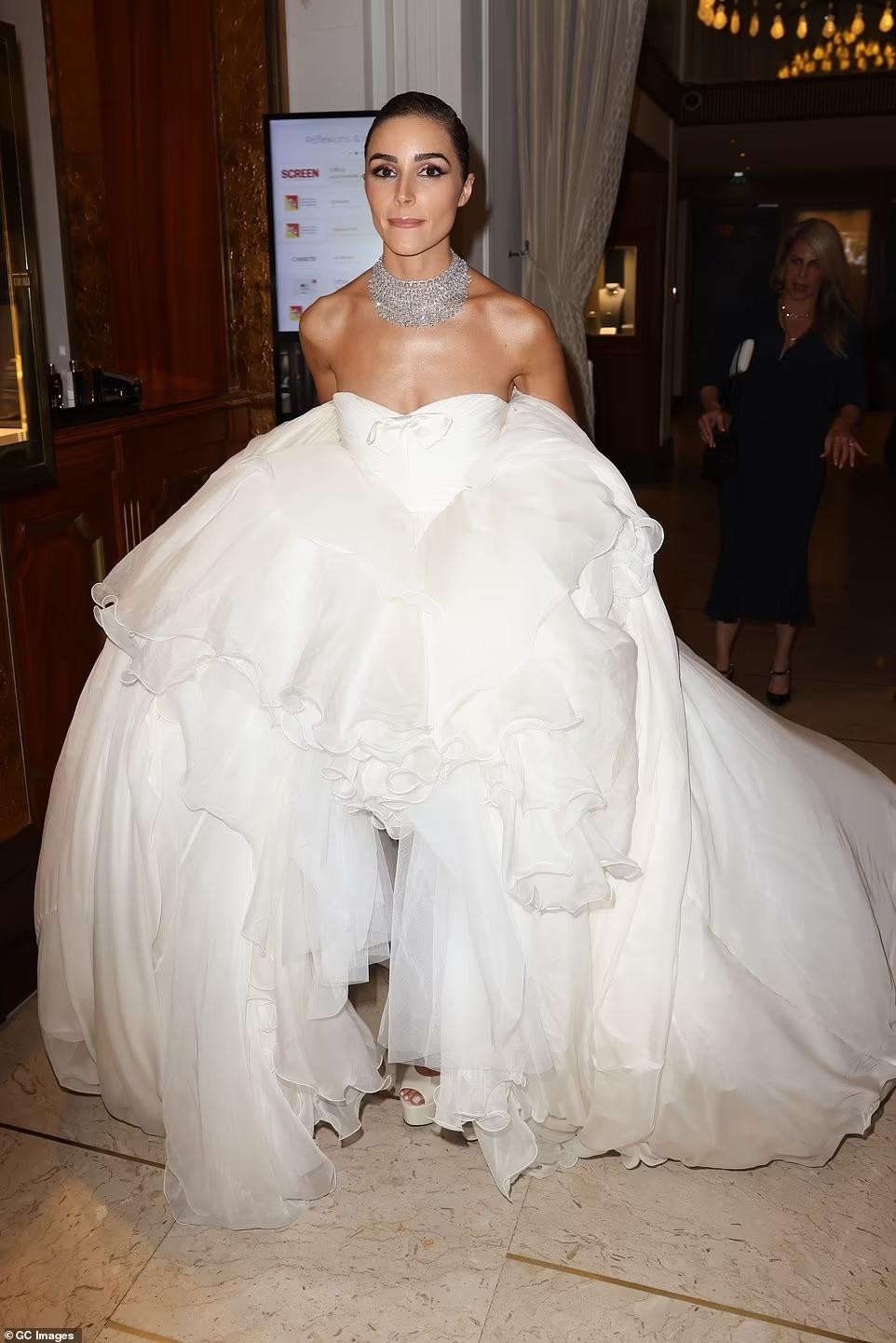 Olivia diện bộ váy màu trắng xếp ly lạ mắt và khá vất vả khi di chuyển tới thảm đỏ.