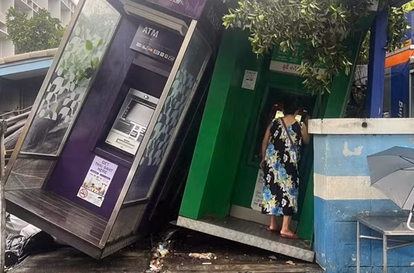 Người phụ nữ vào cây ATM để thực hiện giao dịch dù cây ATM bị nghiêng do mưa dông. Ảnh: Fo UR). Người phụ nữ vào cây ATM để thực hiện giao dịch dù cây ATM bị nghiêng do mưa dông. Ảnh: Fo UR).