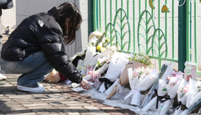 Một người đến đặt hoa trước cổng trường tiểu học, nơi có nữ học sinh bị cô giáo đâm và thiệt mạng. Ảnh: News1. Một người đến đặt hoa trước cổng trường tiểu học, nơi có nữ học sinh bị cô giáo đâm và thiệt mạng. Ảnh: News1.