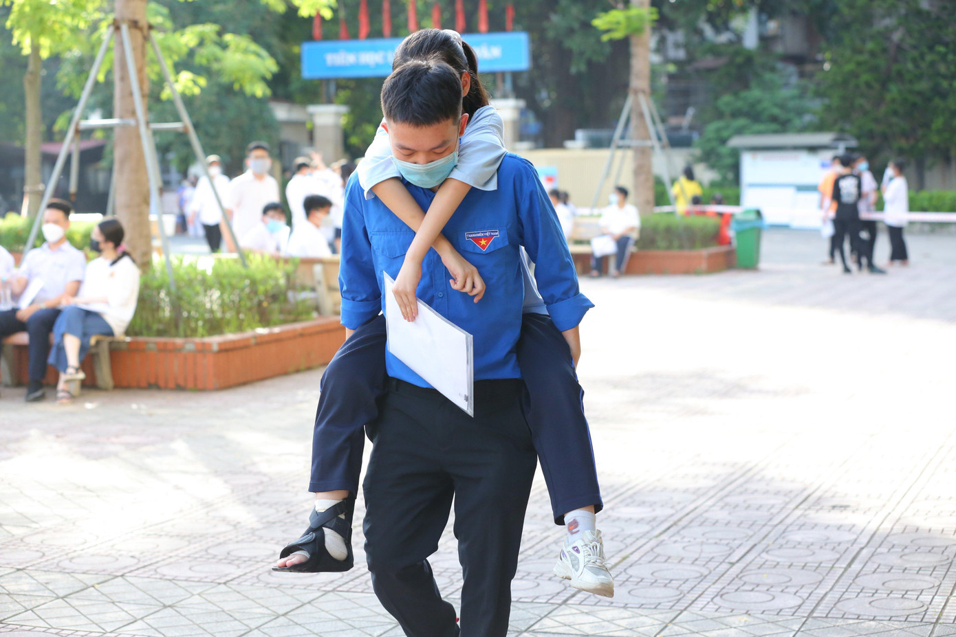 Hoàng Mai Linh THCS Nguyễn Du (Nam Từ Liêm) bị bong gân nên phải bó chân từ 2 tháng nay, bố đưa đến trường, các tình nguyện viên tận tình cõng Linh vào phòng thi số 02 trường THCS Việt Nam - Angieri.