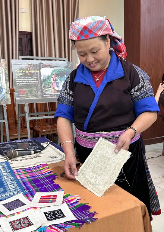 Chị Lý Thị Ninh bên cạnh một tác phẩm được vẽ hoa văn sáp ong trước khi đi đến công đoạn nhuộm chàm. Chị Lý Thị Ninh bên cạnh một tác phẩm được vẽ hoa văn sáp ong trước khi đi đến công đoạn nhuộm chàm.