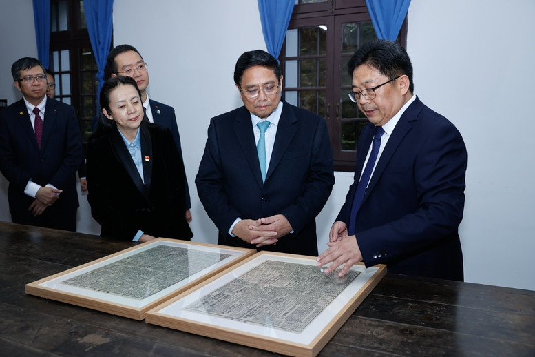 Lãnh đạo Khu Di tích lịch sử Hồng Nham giới thiệu với Thủ tướng Phạm Minh Chính về 2 tờ Tân hoa báo có bài viết của Chủ tịch Hồ Chí Minh khi hoạt động cách mạng tại đây. Ảnh: Nhật Bắc.