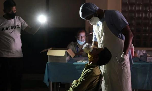 Một nhân viên y tế đang lấy mẫu xét nghiệm cho bệnh nhân dưới ánh đèn pin của điện thoại di động do mất điện. Ảnh: Bloomberg. Một nhân viên y tế đang lấy mẫu xét nghiệm cho bệnh nhân dưới ánh đèn pin của điện thoại di động do mất điện. Ảnh: Bloomberg.