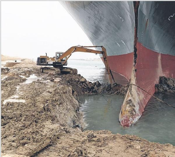 Chiếc máy xúc bé xíu (so với tàu Ever Given) đang cố dọn cát và bùn quanh mũi tàu, khiến nhiều cư dân mạng thấy buồn cười. Ảnh: Straits Times.