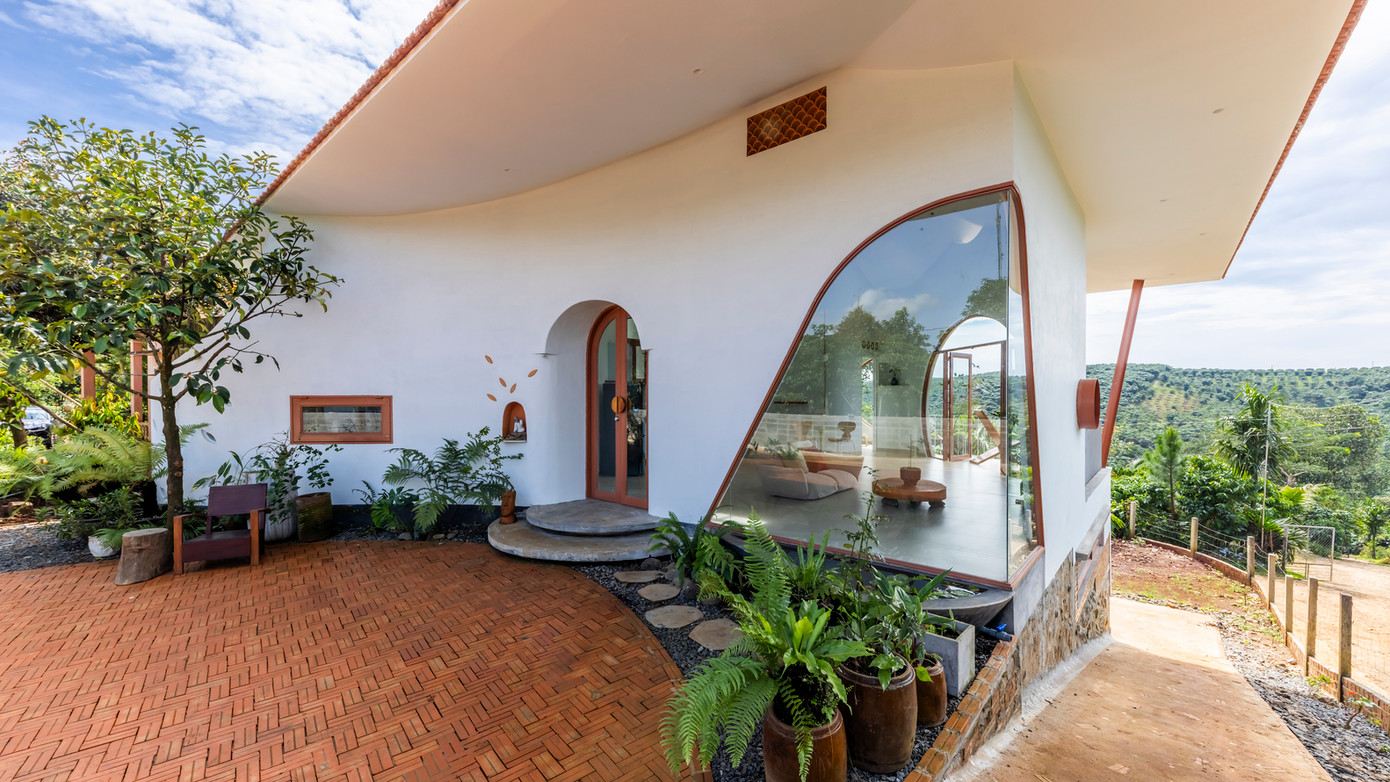 Khu vực xung quanh ngôi nhà được thiết kế chu đáo với sân trong lát gạch đỏ và những tán lá xanh tươi đóng vai trò như rèm cửa tự nhiên, đảm bảo sự riêng tư và mát mẻ.