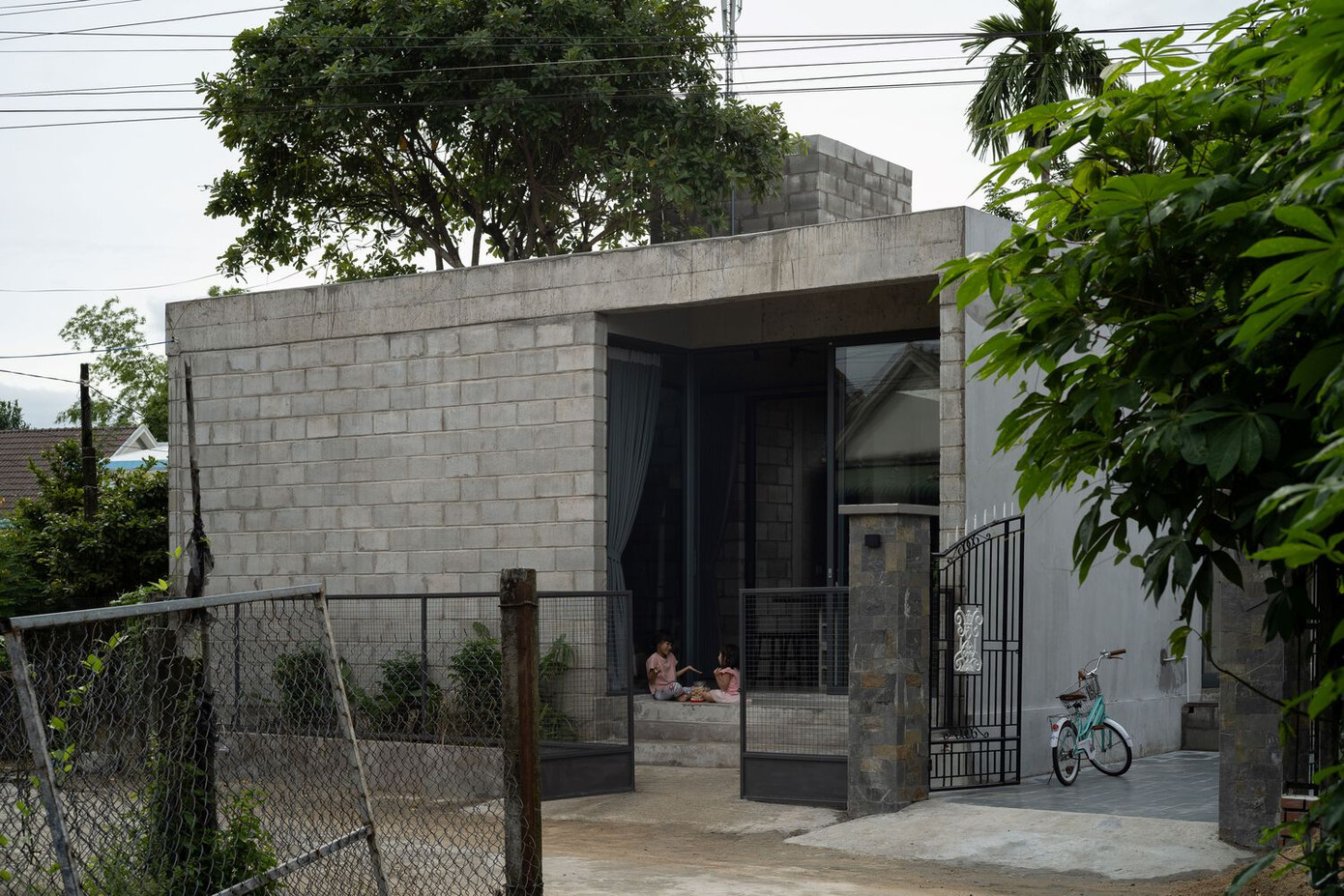 Lối vào chính được bố trí để đảm bảo sự riêng tư, với bức tường khối bê tông chưa hoàn thiện và cửa kính lõm tạo sự tách biệt khỏi đường phố nhưng vẫn duy trì được tầm nhìn từ bên trong.