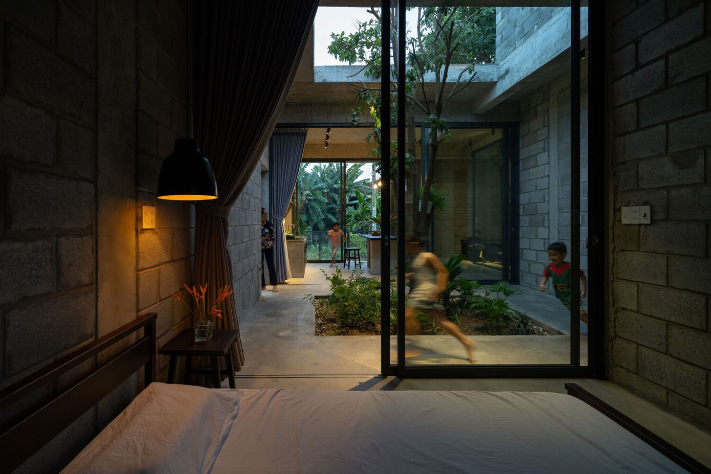 Các cành cây vươn ra qua một lỗ hình chữ nhật trên mái nhà, đưa không gian ngoài trời vào nhà, tăng cường cảm giác rộng mở, cho phép ánh sáng và không khí tự nhiên tràn vào các khu vực sinh hoạt.