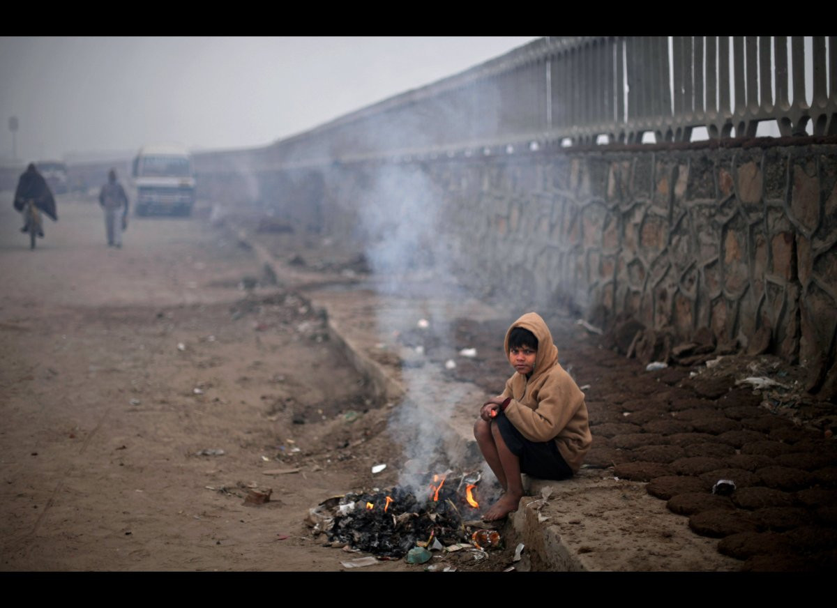 Một cậu bé nghèo khổ ăn mặc phong phanh ngồi bên đống lửa đốt bằng rác ở New Delhi