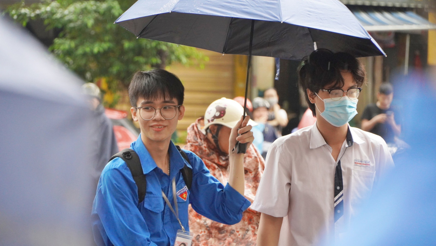 Tình nguyện viên Thủ đô đội mưa che ô cho thí sinh.