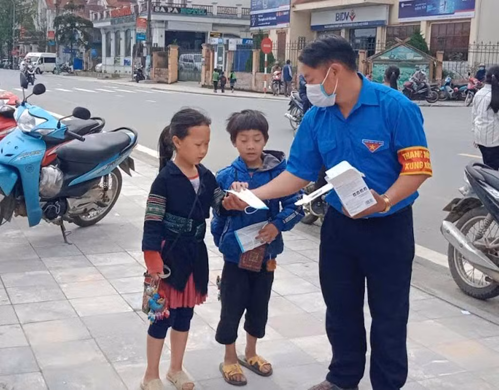 Thào A Dê tuyên truyền phòng chống dịch COVID-19 và phát khẩu trang cho người dân, trẻ em tại địa phương.