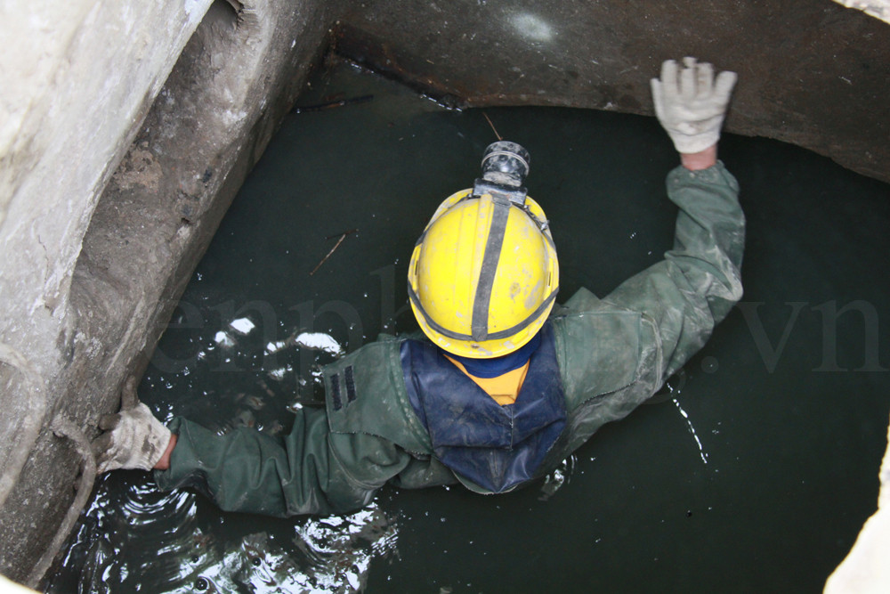 Nước thải ngập đến ngang ngực. Dưới cống không có ánh sáng, phải sử dụng đèn pin. Ảnh: Trường Phong