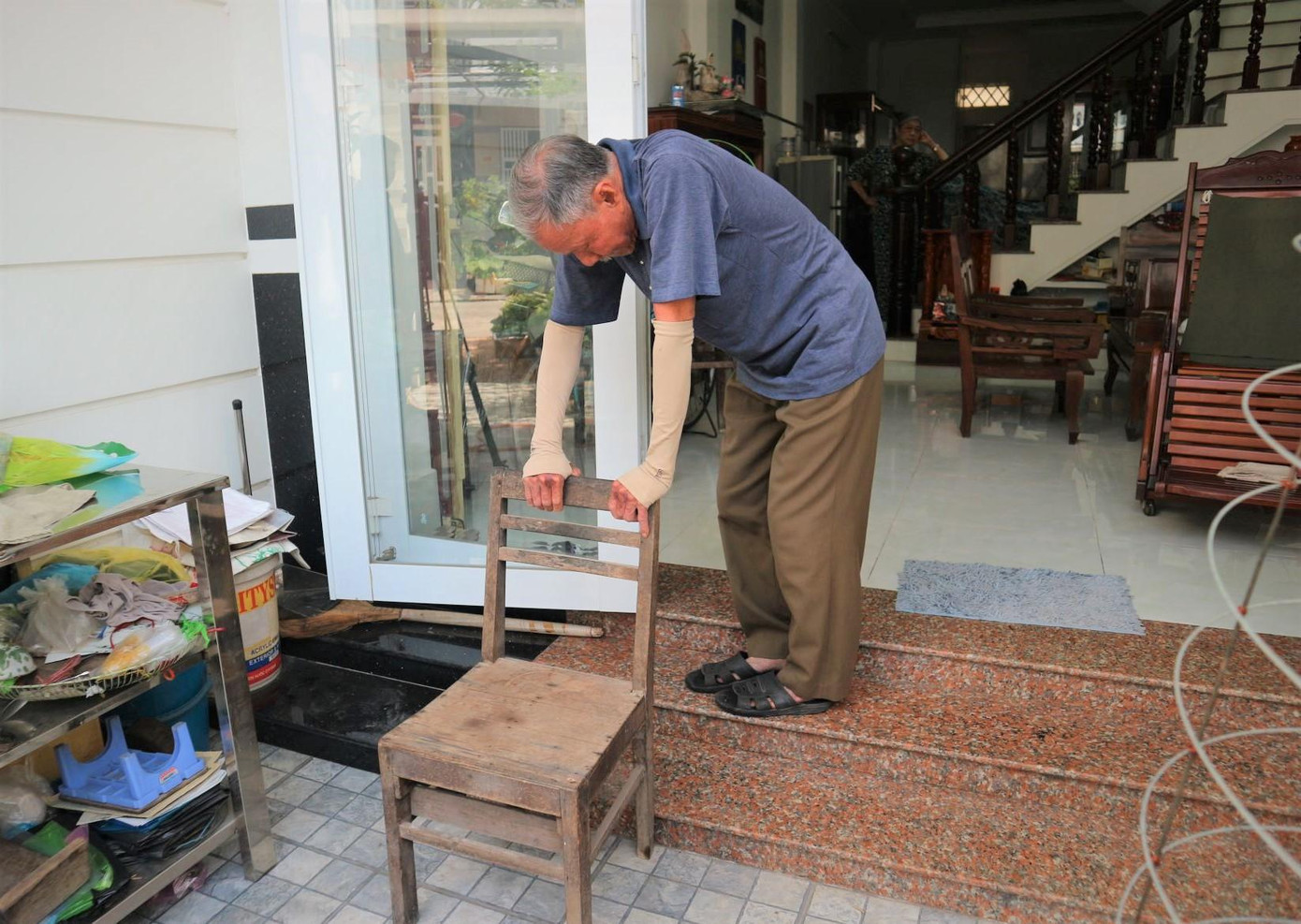 Vì đau nhức, nhiều lúc chú Tấn phải dựa vào ghế khi lên bậc tam cấp.