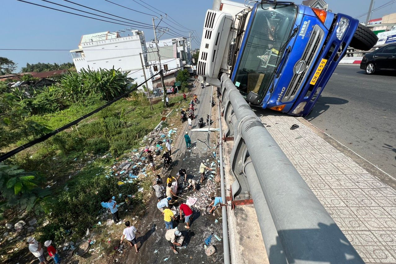 Xe tải chở cá lật nằm đè trên lan can cầu.