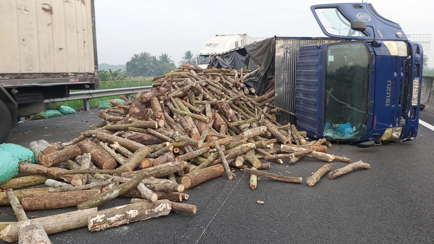 Xe tải bị lật khiến củi trên thùng xe đổ tràn lan xuống đường.