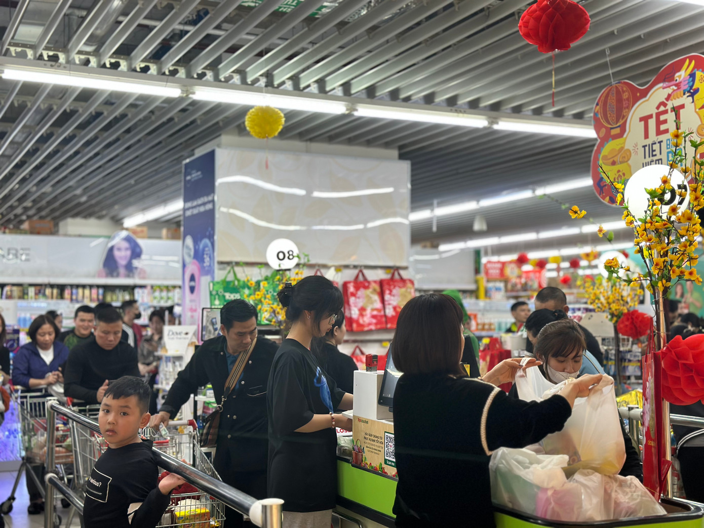 Nhiều em nhỏ theo bố mẹ đi sắm Tết, kiên nhẫn chờ tới lượt thanh toán. Tối 27 Tết, sau 22 giờ, quầy thanh toán của một siêu thị trên đường Lê Trọng Tấn (Thanh Xuân) vẫn chưa ngớt khách. 14 quầy thanh toán của siêu thị hoạt động hết công suất.