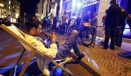 Người đàn ông này ngồi trên ghế trong khi những người khác xếp hàng trước cửa hàng bán lẻ