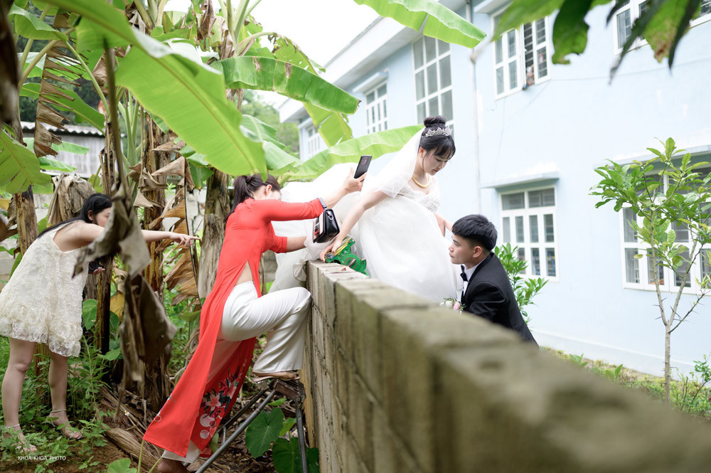 Cô dâu chật vật trèo tường dưới sự giúp đỡ của chú rể và người thân. Cô dâu chật vật trèo tường dưới sự giúp đỡ của chú rể và người thân.