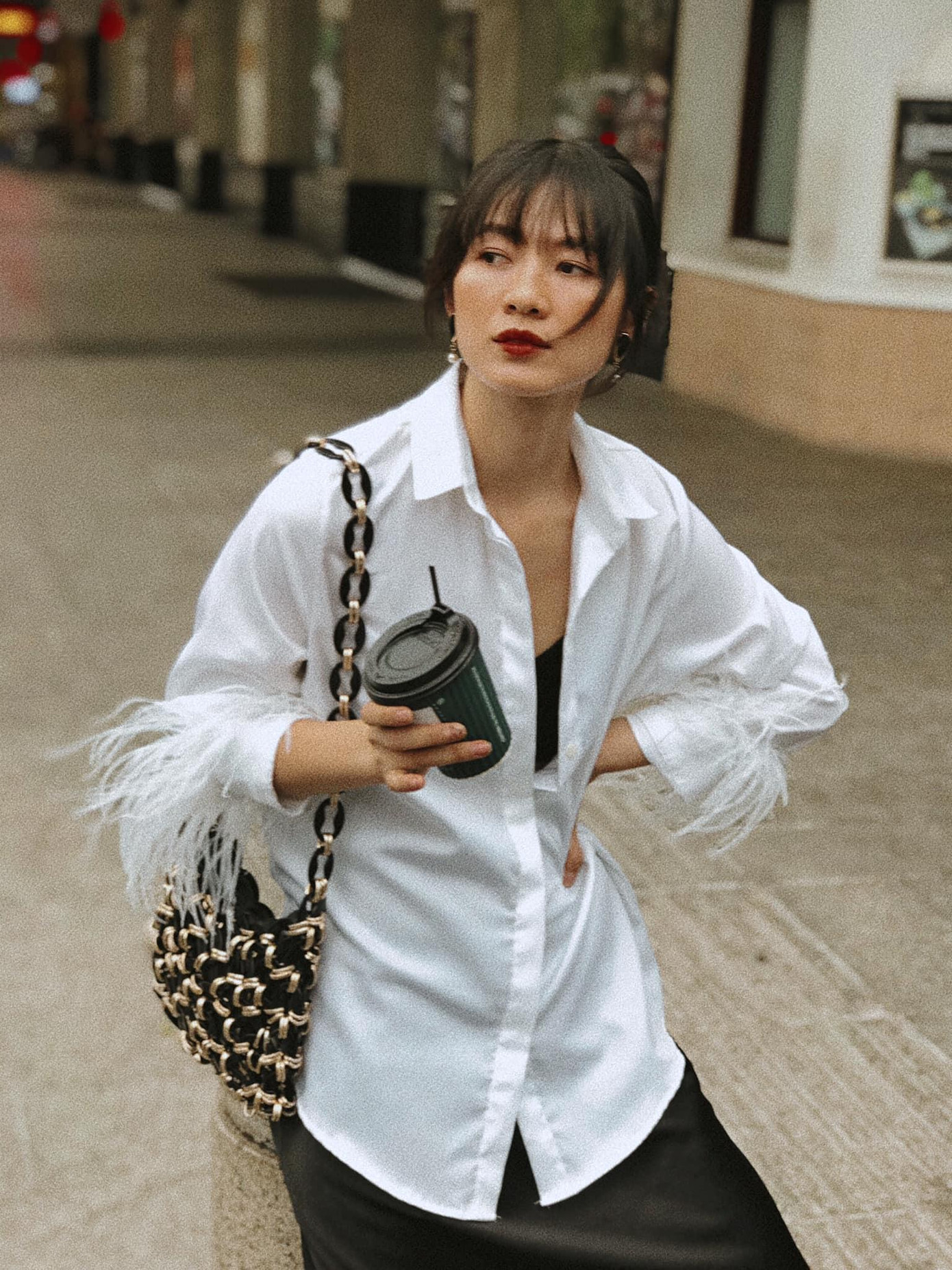 Một chiếc áo sơ mi cách điệu phối với chân váy lụa màu đen kết hợp cùng túi xách kiểu đan móc khiến cô nàng như trở thành một quý cô cổ điển.