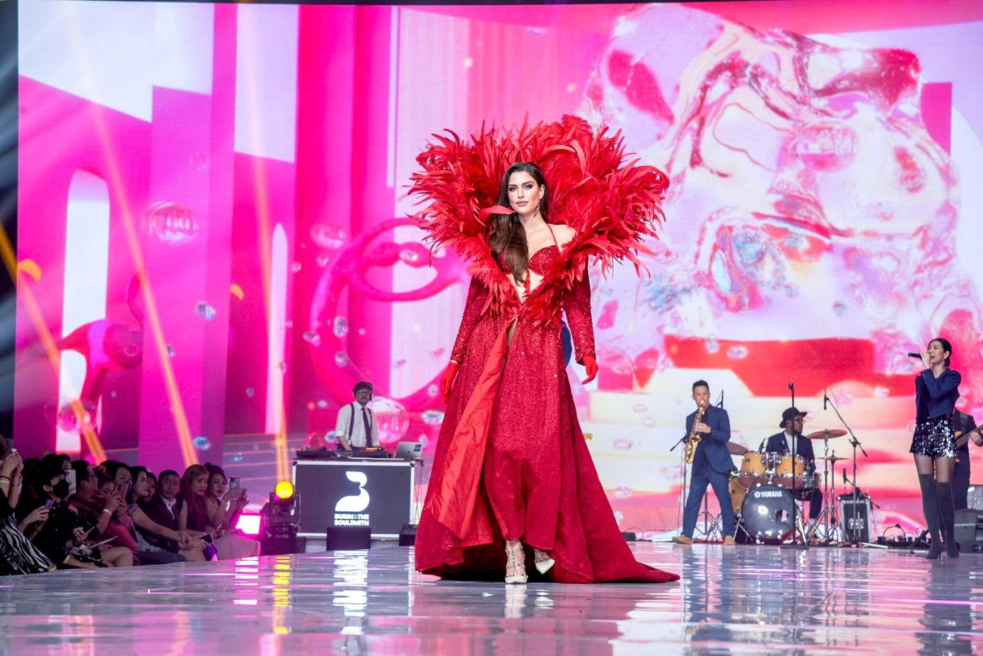 Hoa hậu Hòa bình Quốc tế 2022 Isabella Menin đóng vai trò vedette trong màn trình diễn. Cô diện áo choàng màu đỏ với phần cổ đính lông vũ lộng lẫy, bên trong là bộ bikini cùng tông màu nổi bật, sexy.