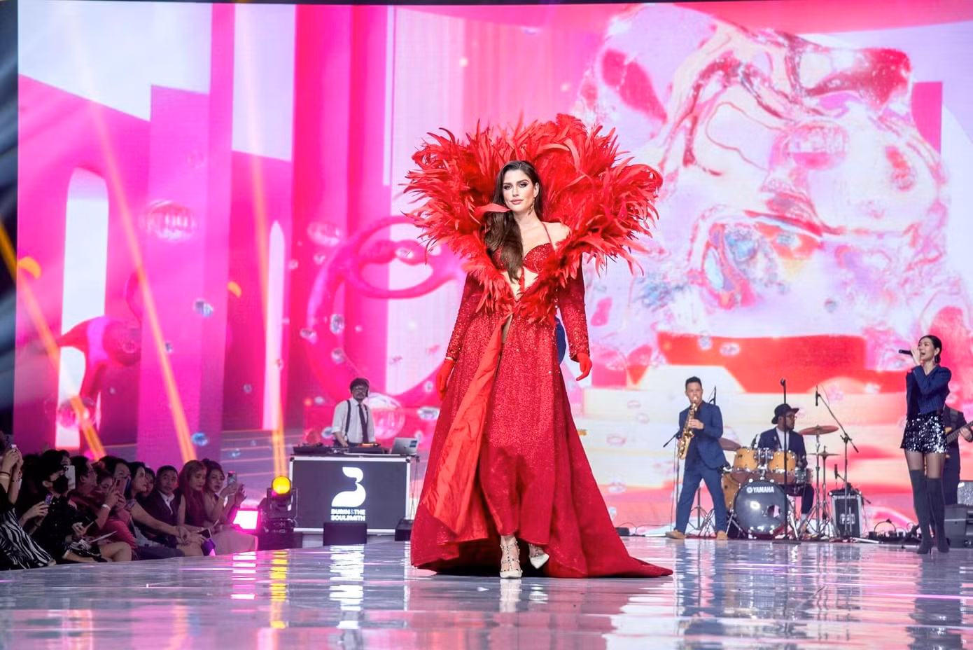 Hoa hậu Hòa bình Quốc tế 2022 Isabella Menin đóng vai trò vedette trong màn trình diễn. Cô diện áo choàng màu đỏ với phần cổ đính lông vũ lộng lẫy, bên trong là bộ bikini cùng tông màu nổi bật, sexy.
