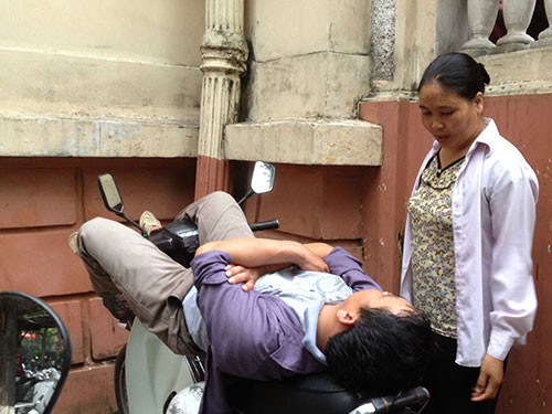 Ngả lưng trên yên xe máy tại khu để xe của nhân viên BV K sau một đêm trắng thức trông người nhà Ảnh: NGỌC DUNG