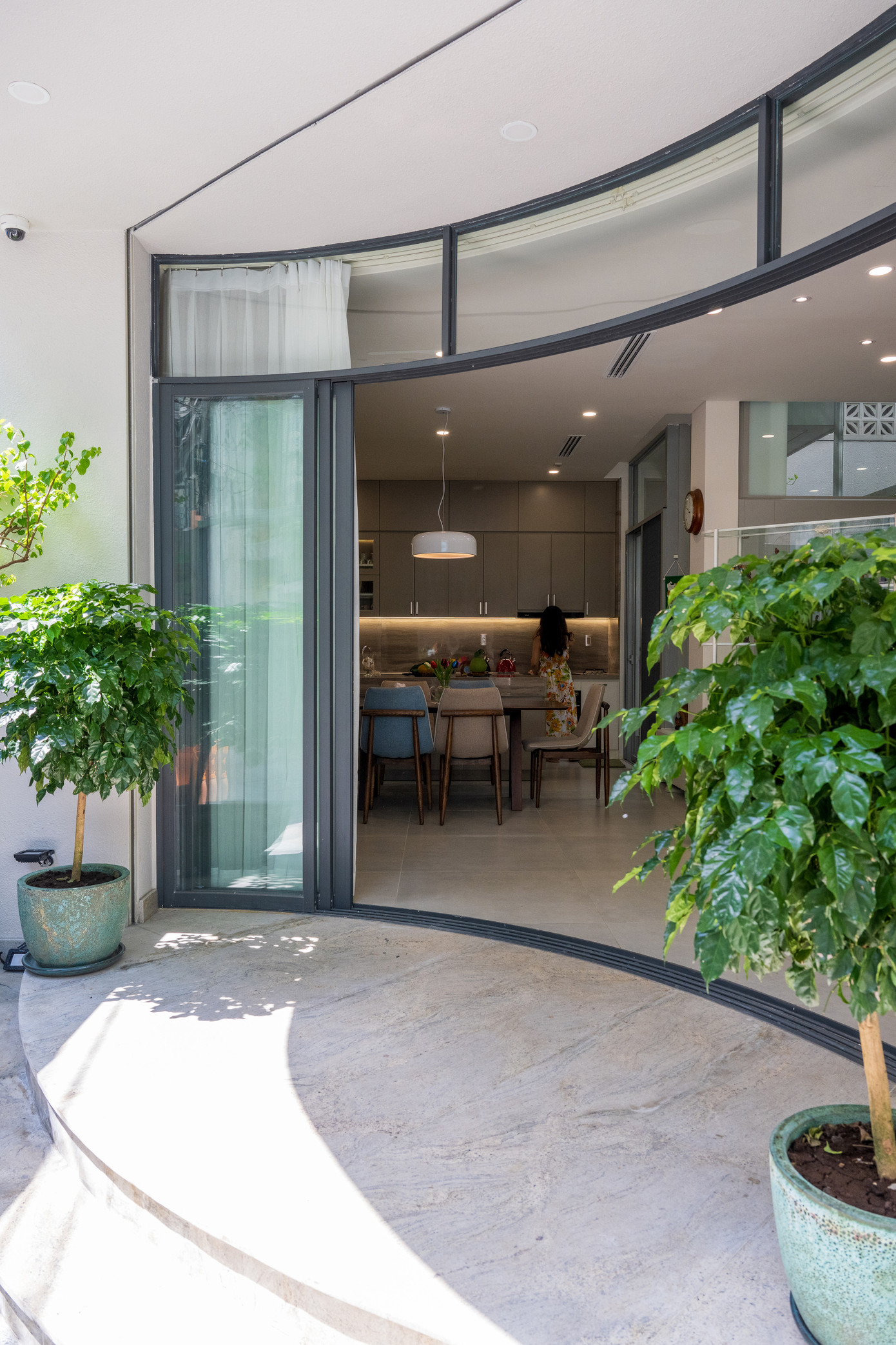 Một khoảng lùi vừa đủ từ góc hẻm được thiết kế để dành chỗ cho lối vào và khoảng sân giản dị trước nhà. Bậc tam cấp bằng đá granite được tạo hình uốn cong hướng ra sân và hệ cửa kính lớn cong lõm vào trong tạo ra một khoảng hiên nhà hình elip độc đáo ở tầng trệt. Một khoảng lùi vừa đủ từ góc hẻm được thiết kế để dành chỗ cho lối vào và khoảng sân giản dị trước nhà. Bậc tam cấp bằng đá granite được tạo hình uốn cong hướng ra sân và hệ cửa kính lớn cong lõm vào trong tạo ra một khoảng hiên nhà hình elip độc đáo ở tầng trệt.