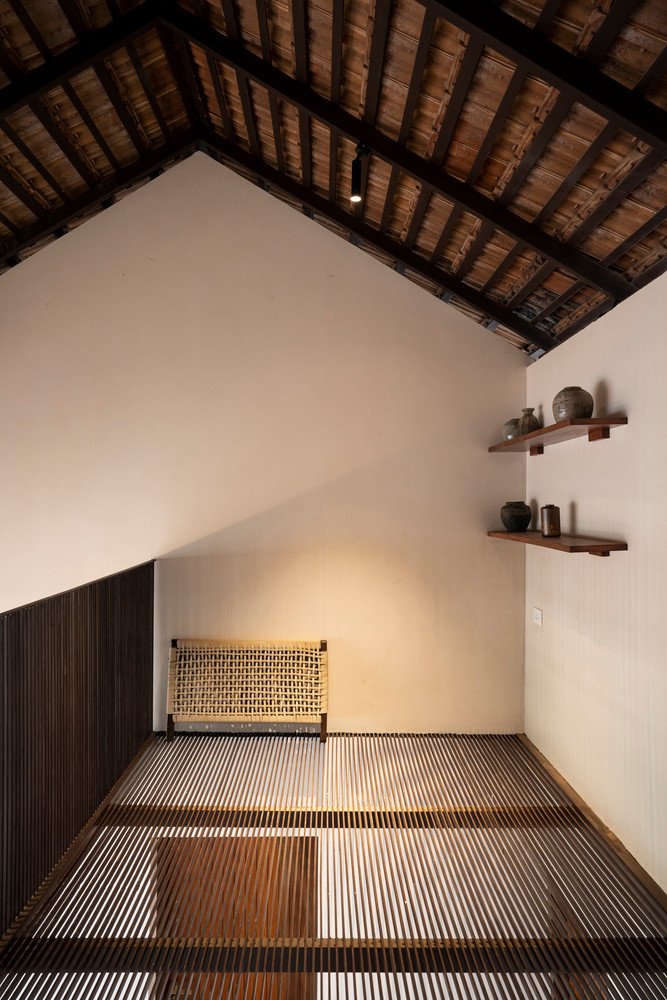 Cửa có mái che bằng gỗ theo phong cách truyền thống ở mặt tiền, sàn bê tông kết hợp khảm đá trên tường trong khi đồ nội thất được thiết kế theo phong cách xưa cũ.